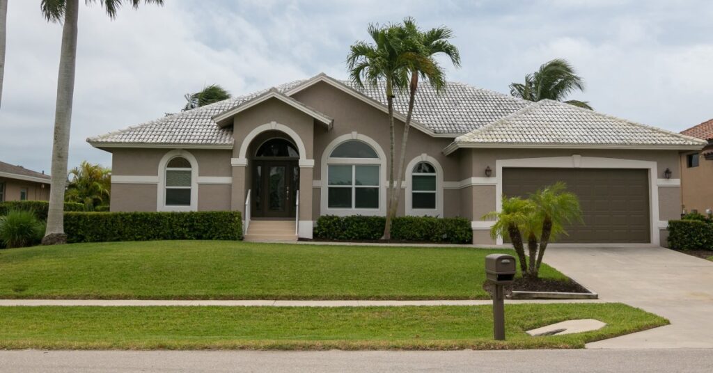 The outside of a beautiful, beige Florida home. The house has white trim along it and has large arch doorway and windows.