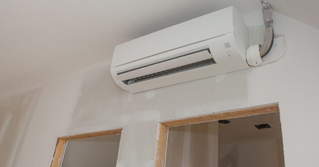 A white, wall-mounted mini-split installed above an unfinished doorway inside of an otherwise empty property.