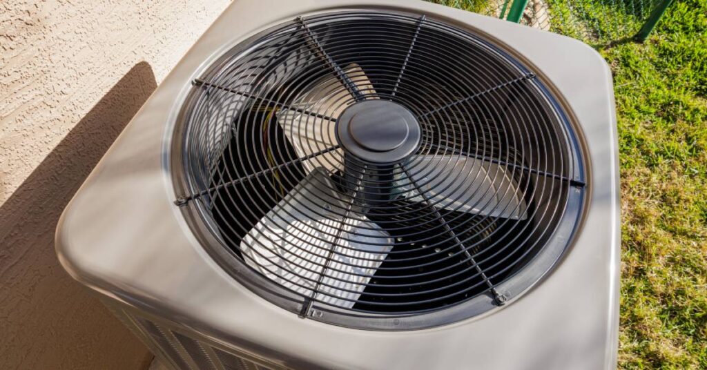 The top of a clean, outdoor HVAC unit that’s beside a residential property and a green chain-link fence.