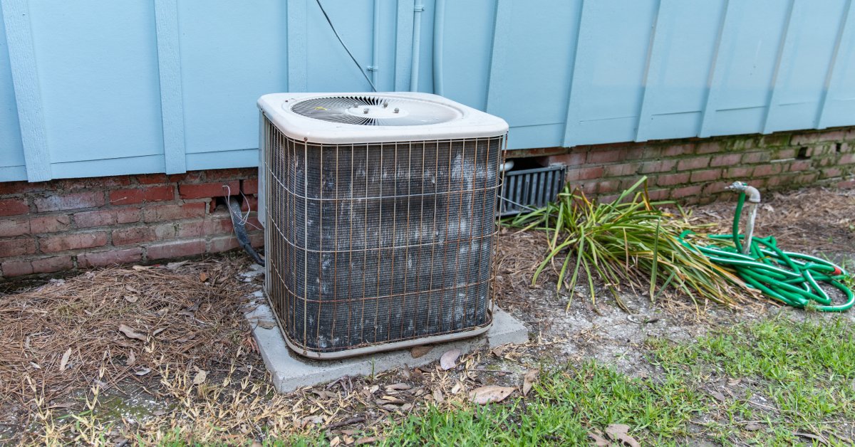 An outdoor AC unit sits on a concrete slap beside a blue home. Dirt and grime covers the outside air conditioner.