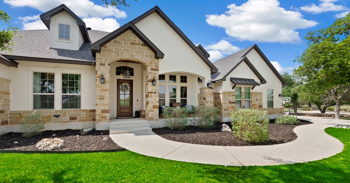 A curved walkway leads to the front of a home with cream-colored concrete walls and light brown brickwork.