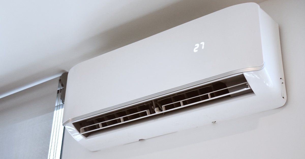 An indoor mini-split with the number twenty-seven displayed on it is mounted to the top of a wall beside a window.