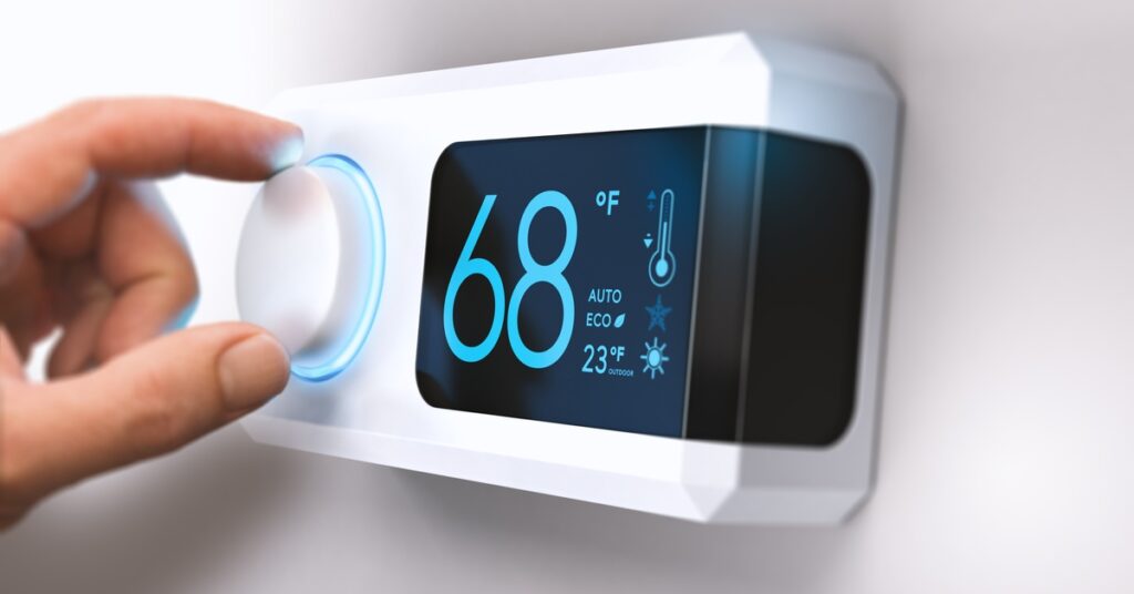 A person’s forefinger and thumb on the temperature knob of a thermostat that is set to 68 degrees Fahrenheit.