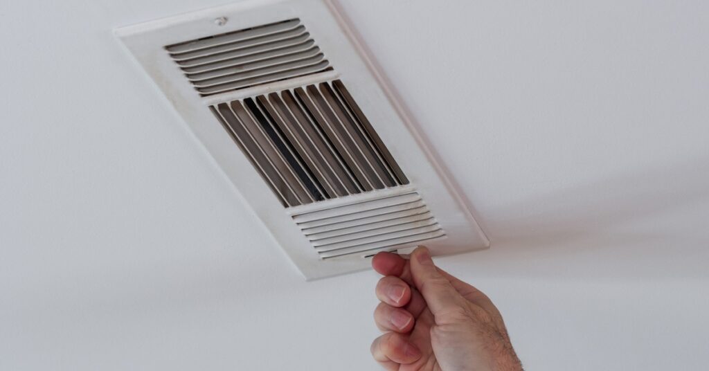 A close-up of a person’s hand reaching up and touching the sliding switch of a white ceiling vent.