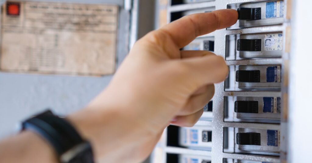 A close up of a hand with the finger on one of the many black switches of a residential circuit breaker.