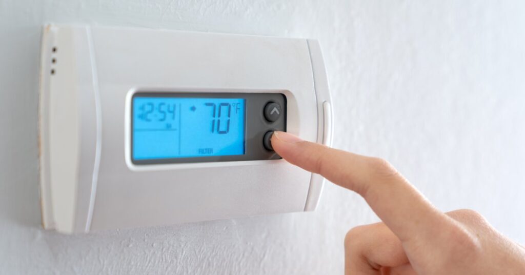 A person’s finger rests on the decrease button of a wall-mounted thermostat that’s currently set to 70 degrees Fahrenheit.