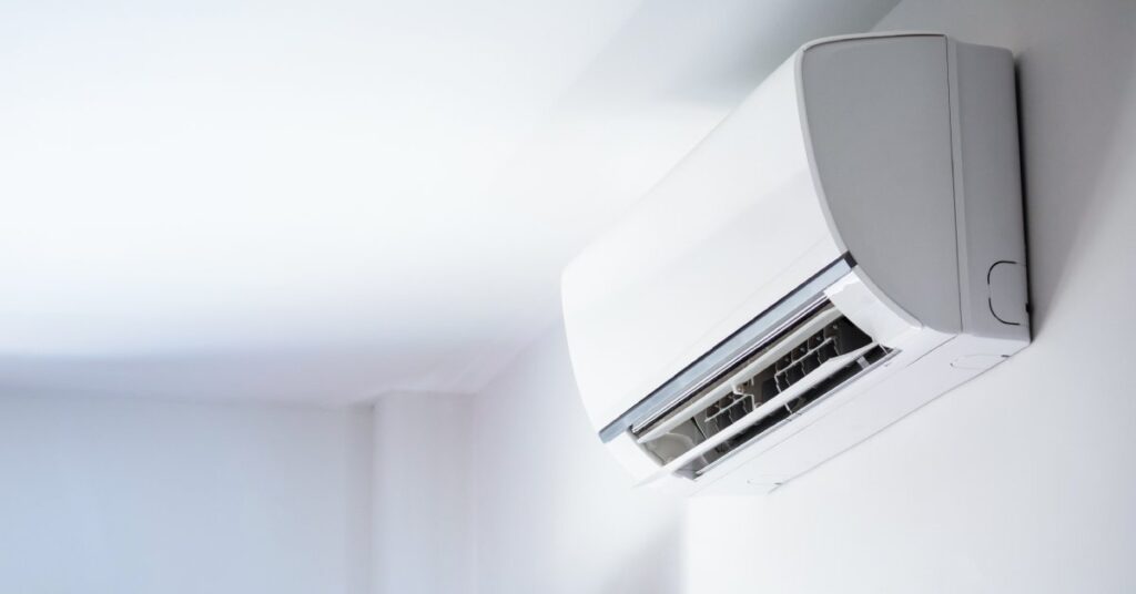 A white ductless mini-split mounted on a white wall near a corner and up close to the ceiling.