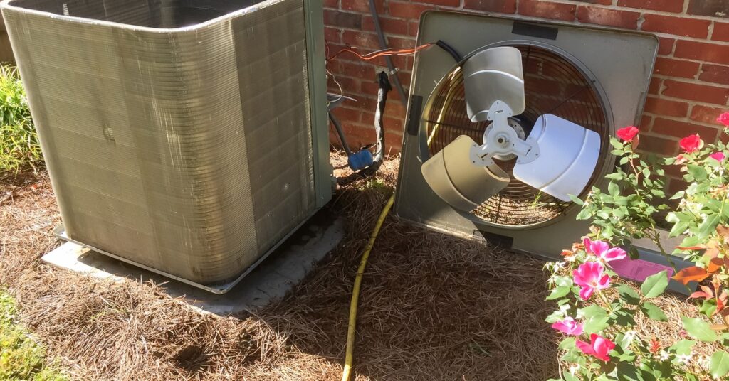 An outdoor AC system beside a brick home sits by itself with the top removed and resting against the house.