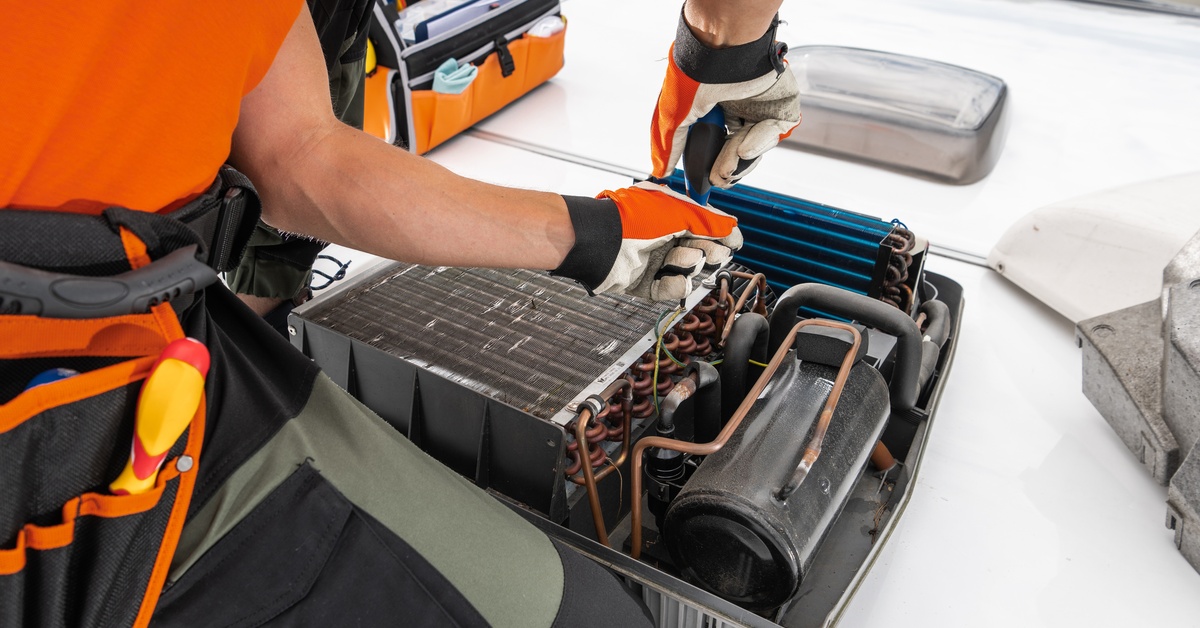 An out-of-view person has the side panel of an AC system on the ground, exposing the condenser coils.