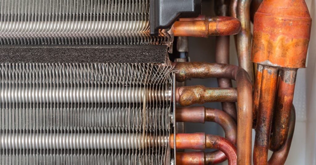 A close-up of condenser coils inside an air-conditioning system. The coils are slightly rusted around the edges.