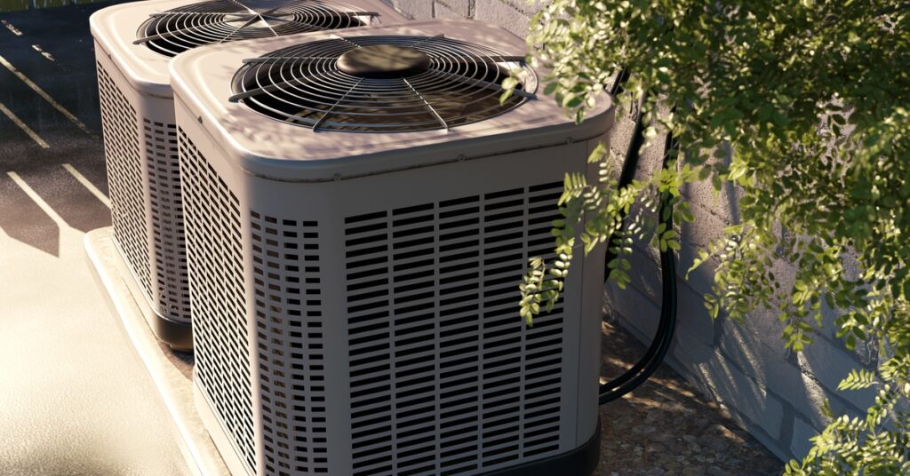 A side view of two outdoor HVAC systems sitting beside each other. They are on a concrete slab and beside a white brick wall.